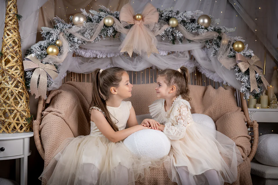 Două fetițe privindu-se zâmbind, între funde de tul și globuri aurii — ședință foto de Crăciun pentru copii în Oradea