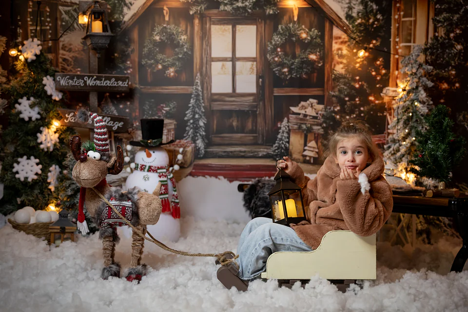 Fetiță în săniuță de lemn cu felinar, lângă ren și om de zăpadă, în fața căsuței lui Moș Crăciun — studio foto Oradea