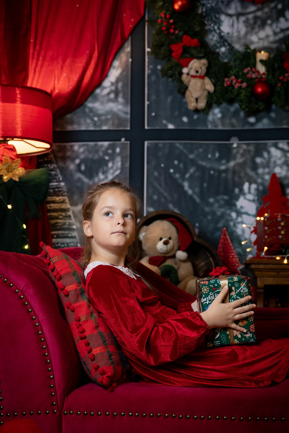 Fetiță în rochiță roșie, întinsă pe canapeaua de catifea cu un cadou în brațe — fotografie de Crăciun în studio, Lavinia Pavel Photography