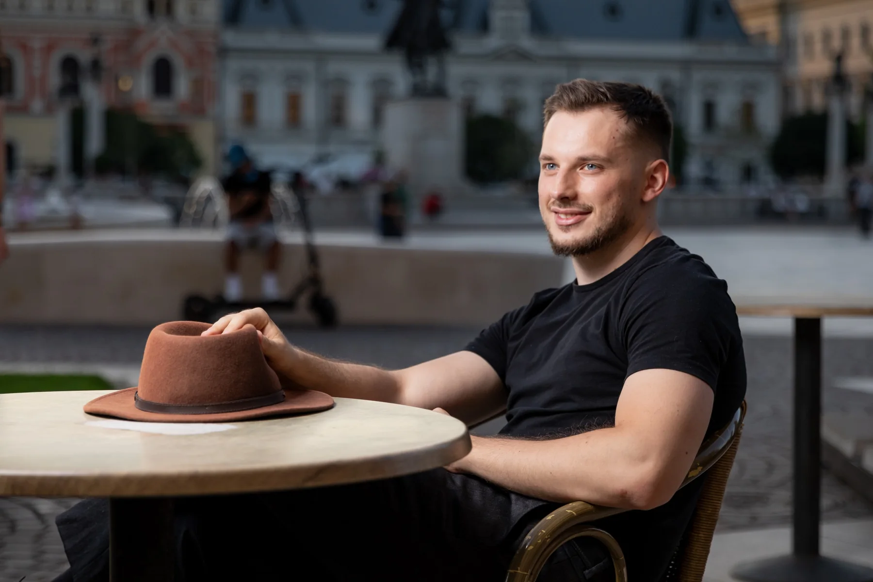 Portret zâmbind la o masă de terasă, cu pălăria pe masă — ședință foto în centrul Oradiei