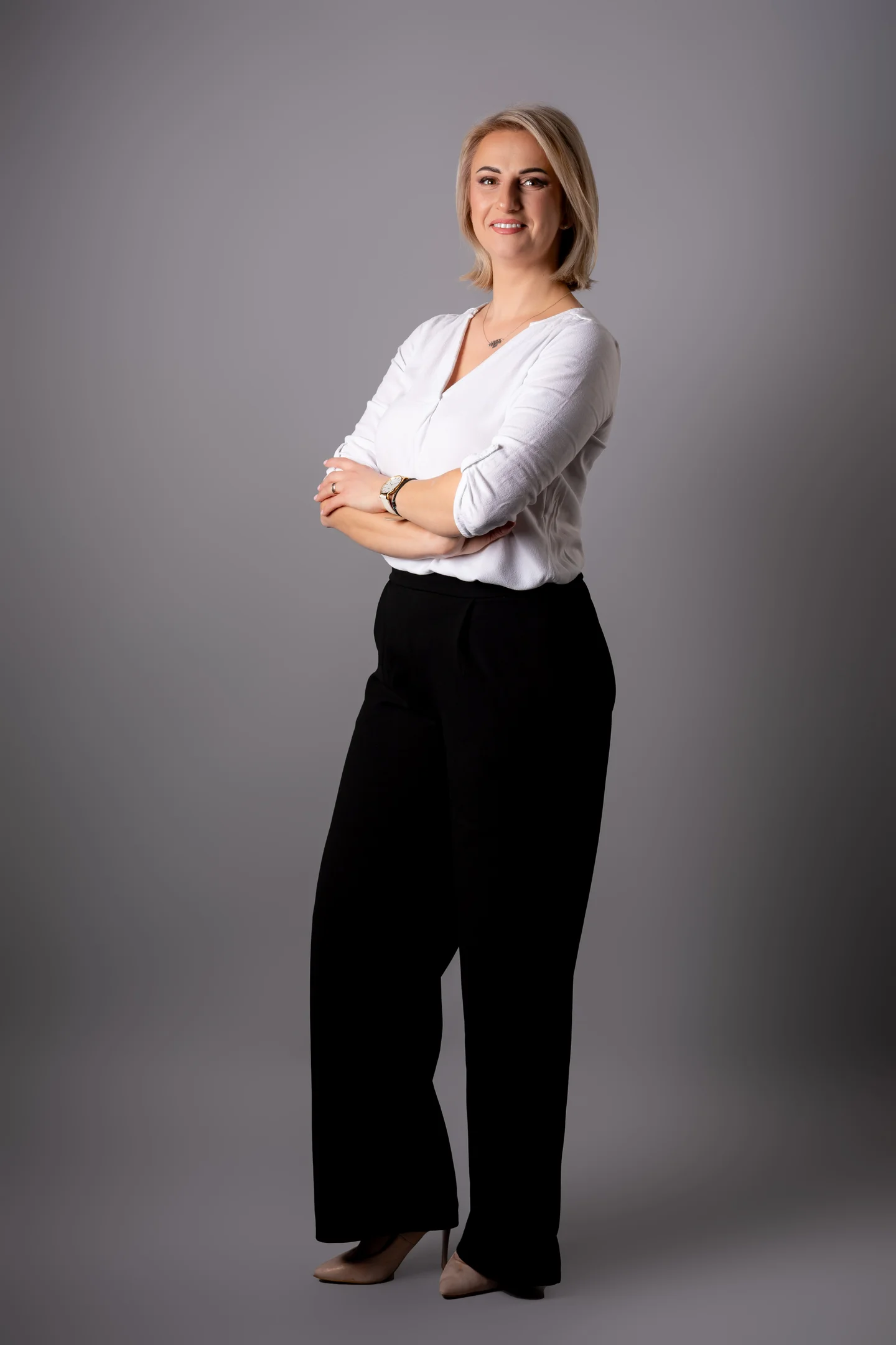 Portret în picioare, în bluză albă și pantaloni negri, pe fundal gri — fotografie business în Oradea