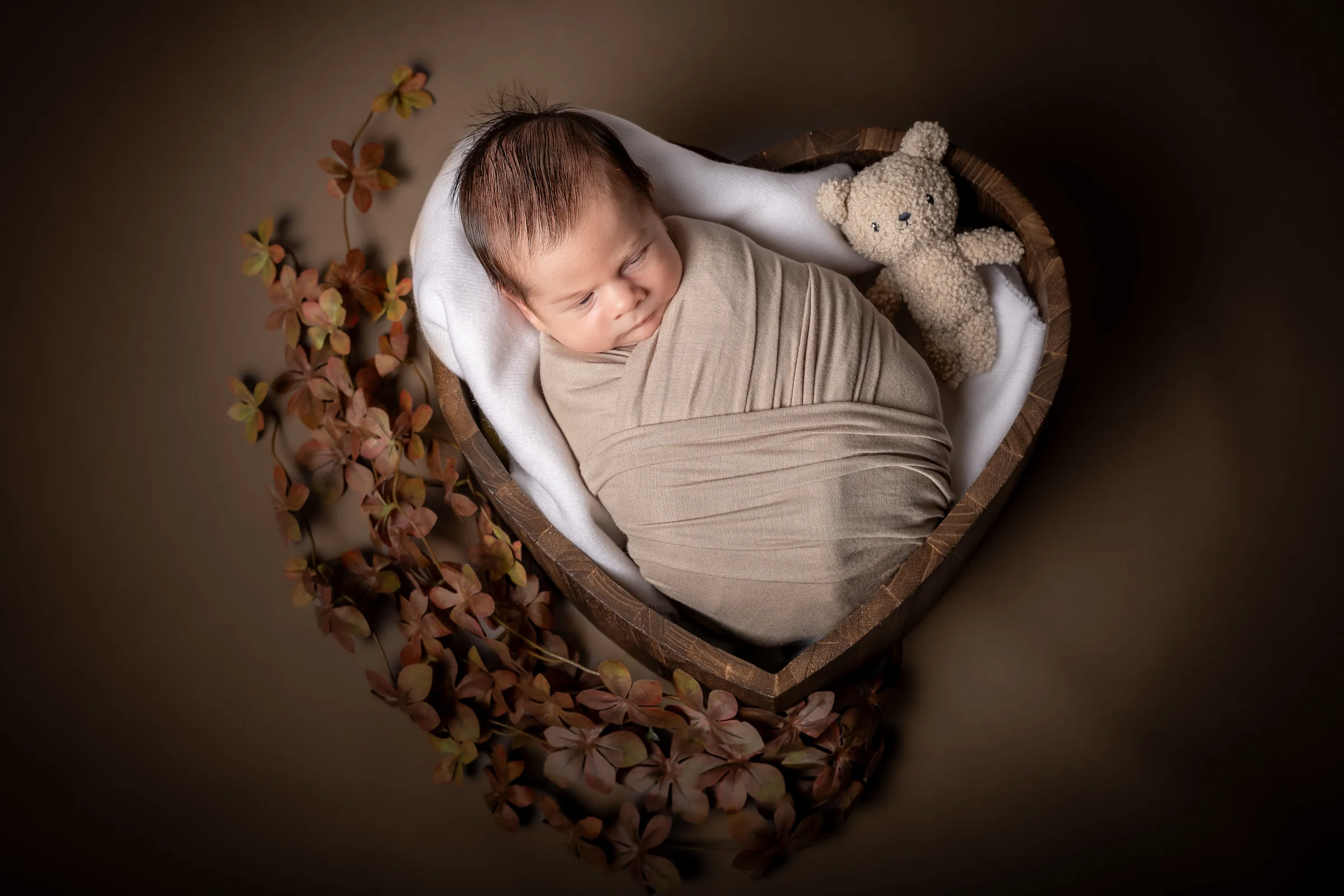 Nou-născut adormit într-un coș decorat cu frunze, alături de un ursuleț — fotograf newborn Oradea
