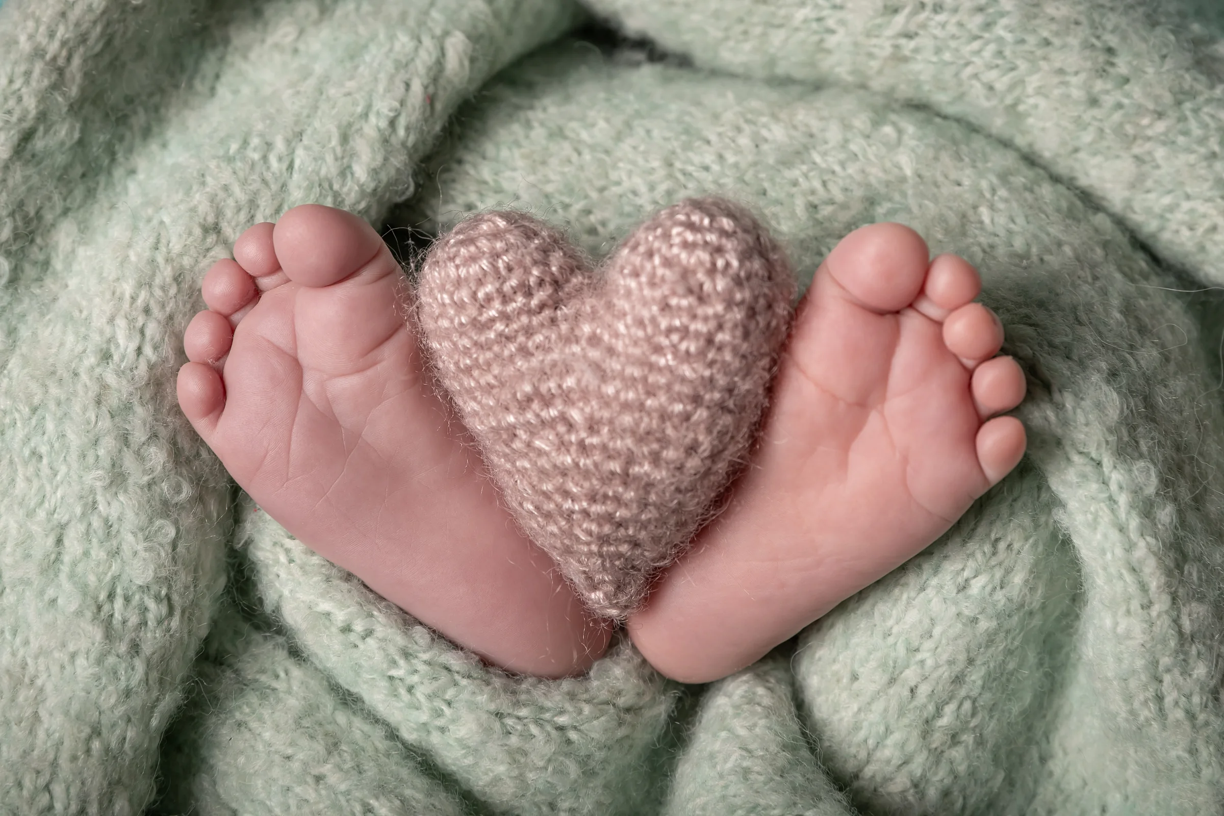 Piciorușele nou-născutului încadrând o inimă tricotată — detaliu din ședință foto newborn