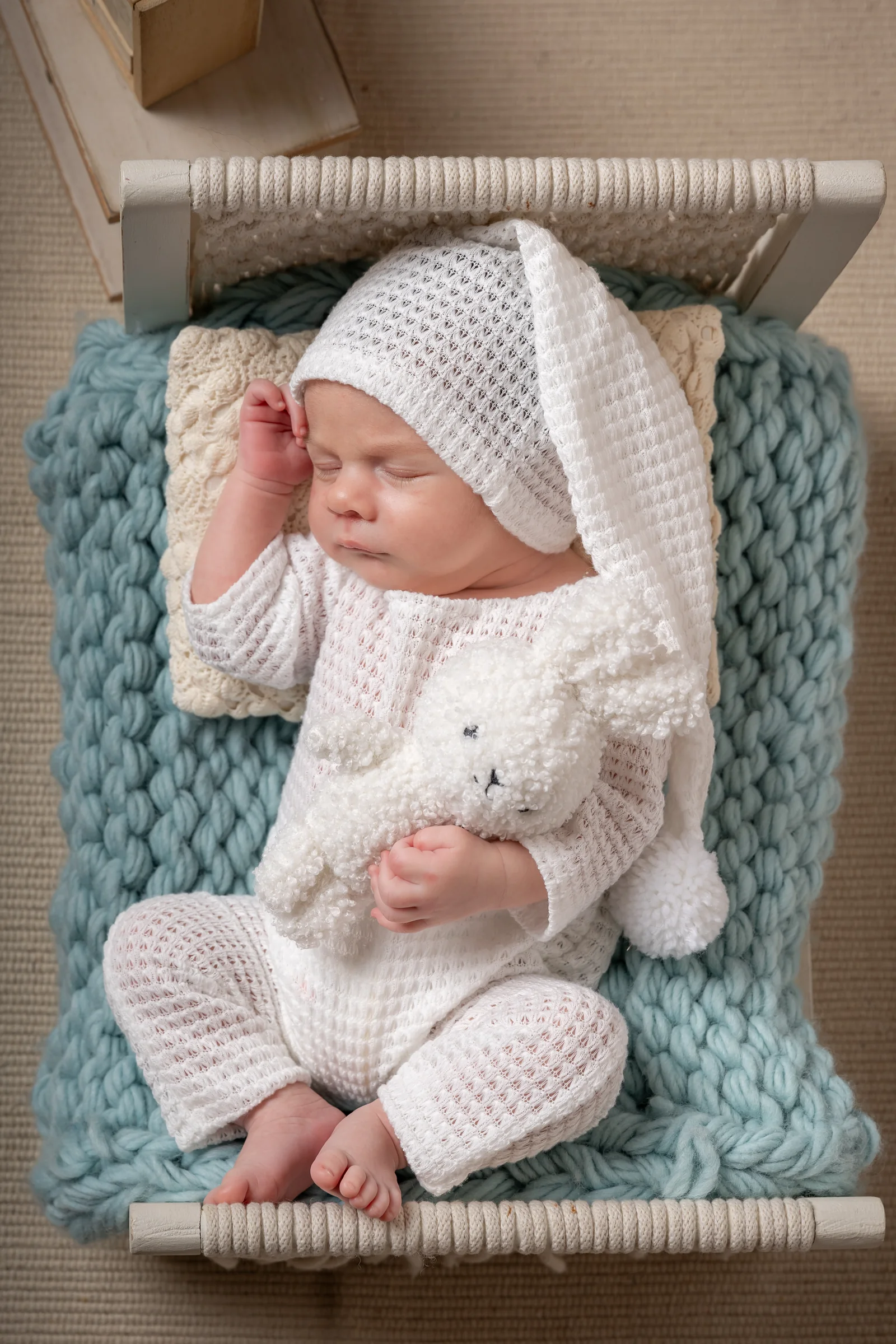 Bebeluș adormit în costumaș alb tricotat, fotografiat de sus — ședință newborn în studio