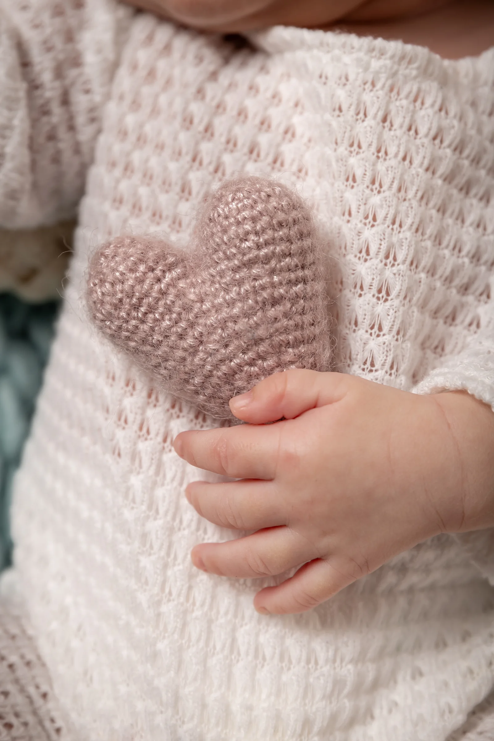 Mâinile bebelușului ținând o inimă tricotată — detaliu delicat din ședința newborn