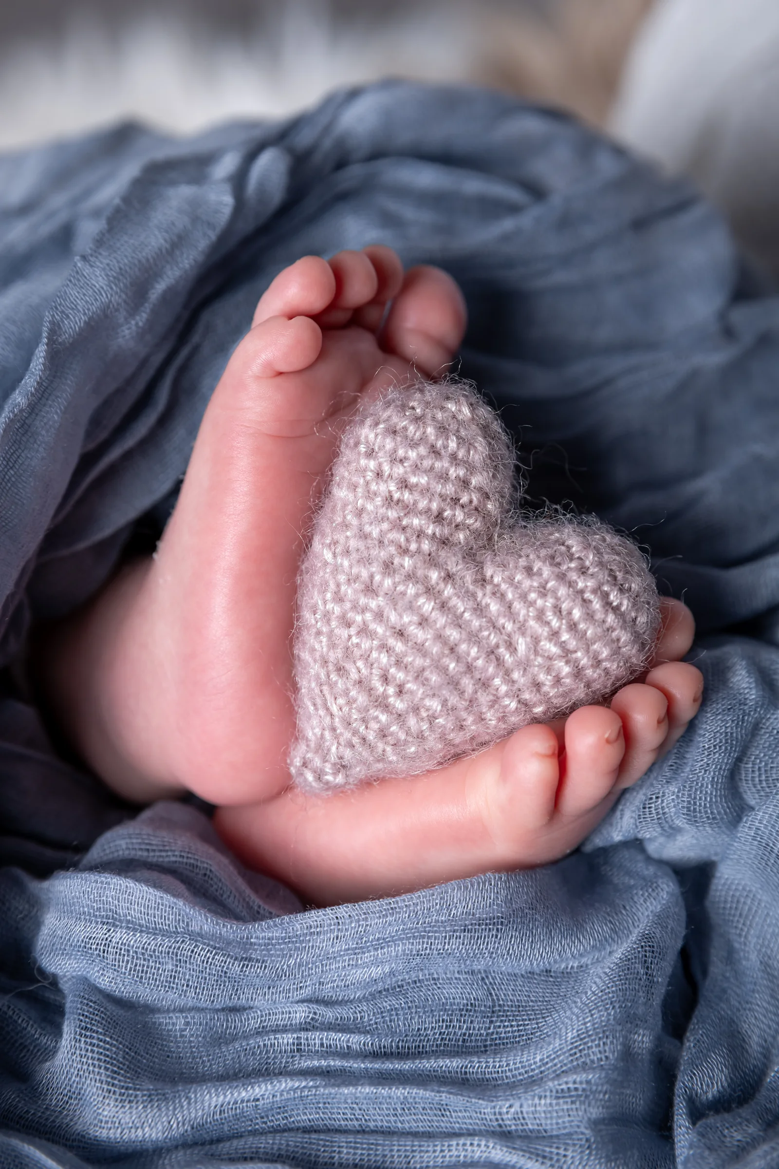 Piciorușele nou-născutului lângă o inimă tricotată, pe pătură albastră — fotografie newborn Oradea