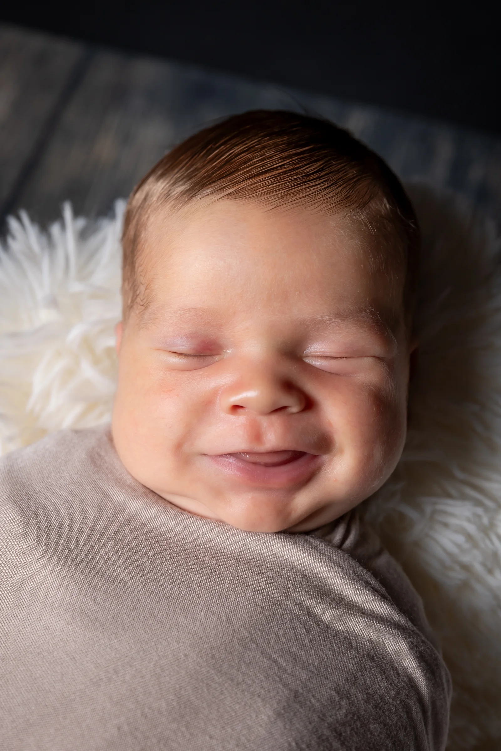 Nou-născut zâmbind în somn, înfășurat într-o pătură moale — fotograf newborn Oradea