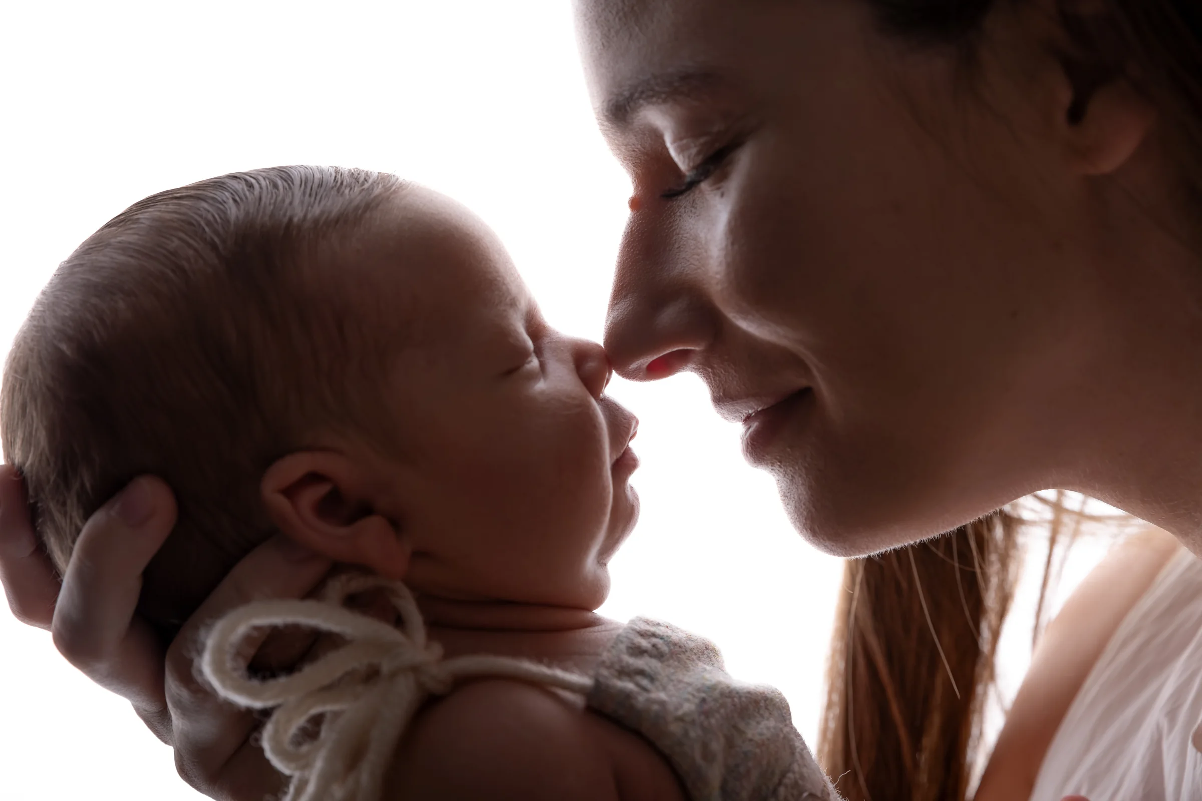 Mamă apropiindu-și chipul de nou-născut, în lumină naturală — ședință newborn Oradea
