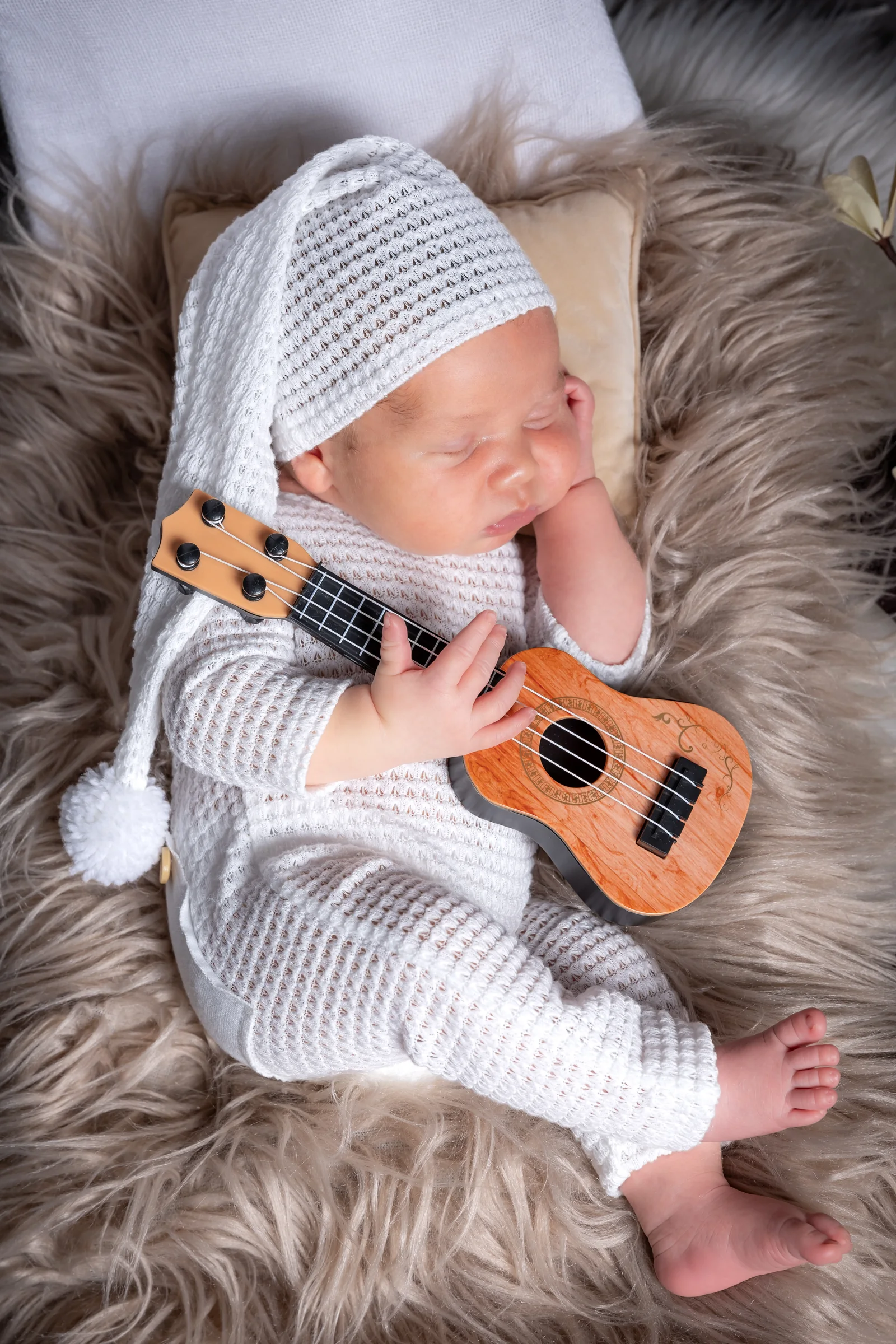 Nou-născut în costumaș alb, ținând o chitară în miniatură — fotografie newborn creativă