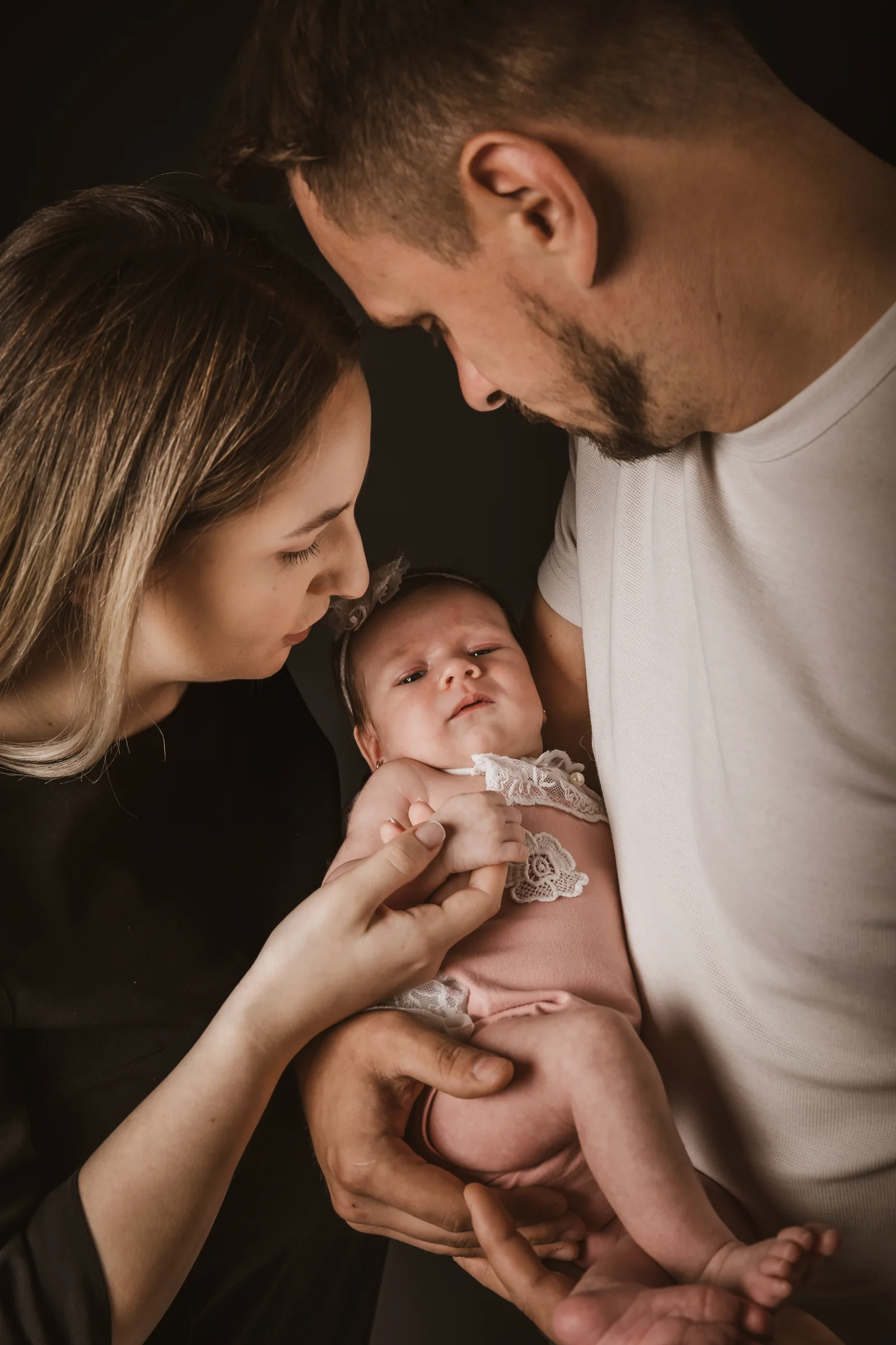 Părinți ținând nou-născutul în brațe, portret în lumină caldă — ședință newborn Oradea