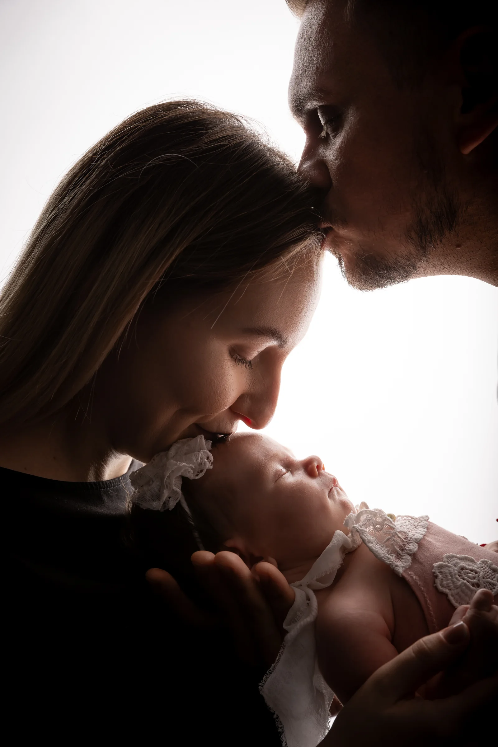 Părinți sărutând nou-născutul, portret emoțional în contralumină — ședință newborn