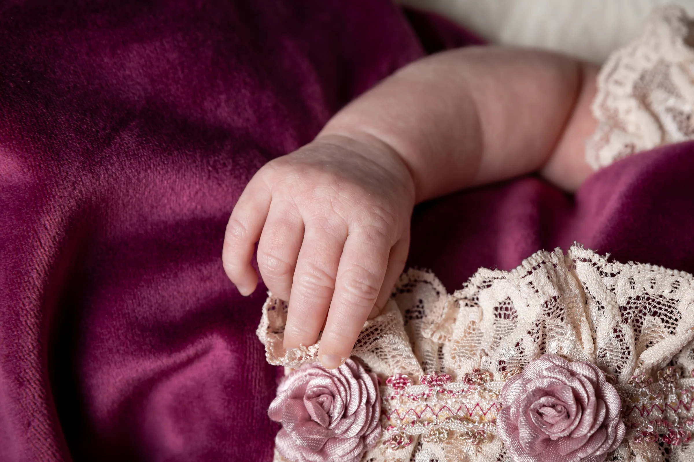 Detaliu cu mâna bebelușului și florile rochiței — fotografie delicată de bebeluș